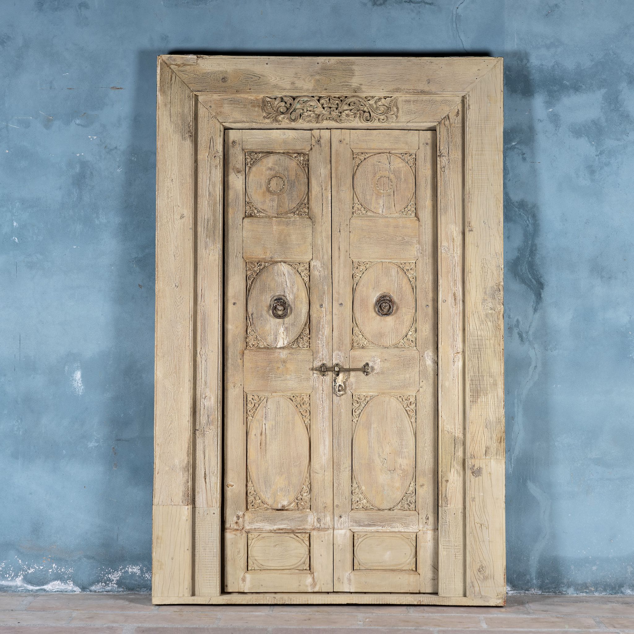 Heavy reclaimed Indian teak door with unique hand carvings, sandblasted finish, and original brass hardware, extended to fit European height within a restored frame.