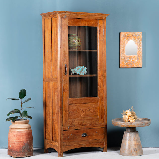 Side angle image of an antique reclaimed teak wood display cabinet with glass door, honey wax finish, and lower drawer – unique furniture showcasing traditional Indian craftsmanship.