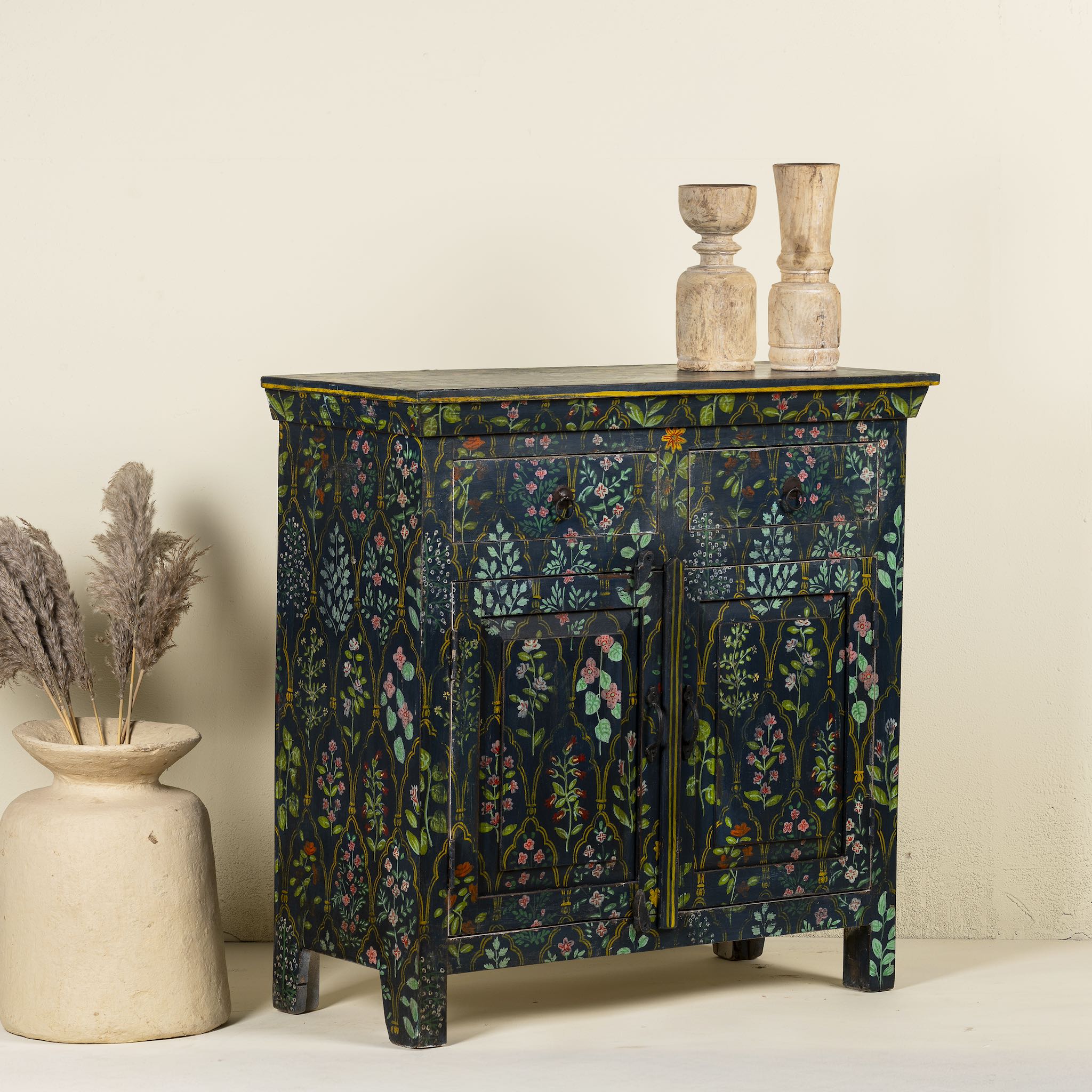 Side angle image of a hand painted cupboard made from recycled wood with floral motifs, two drawers and two doors, 90 × 90 × 40 cm.