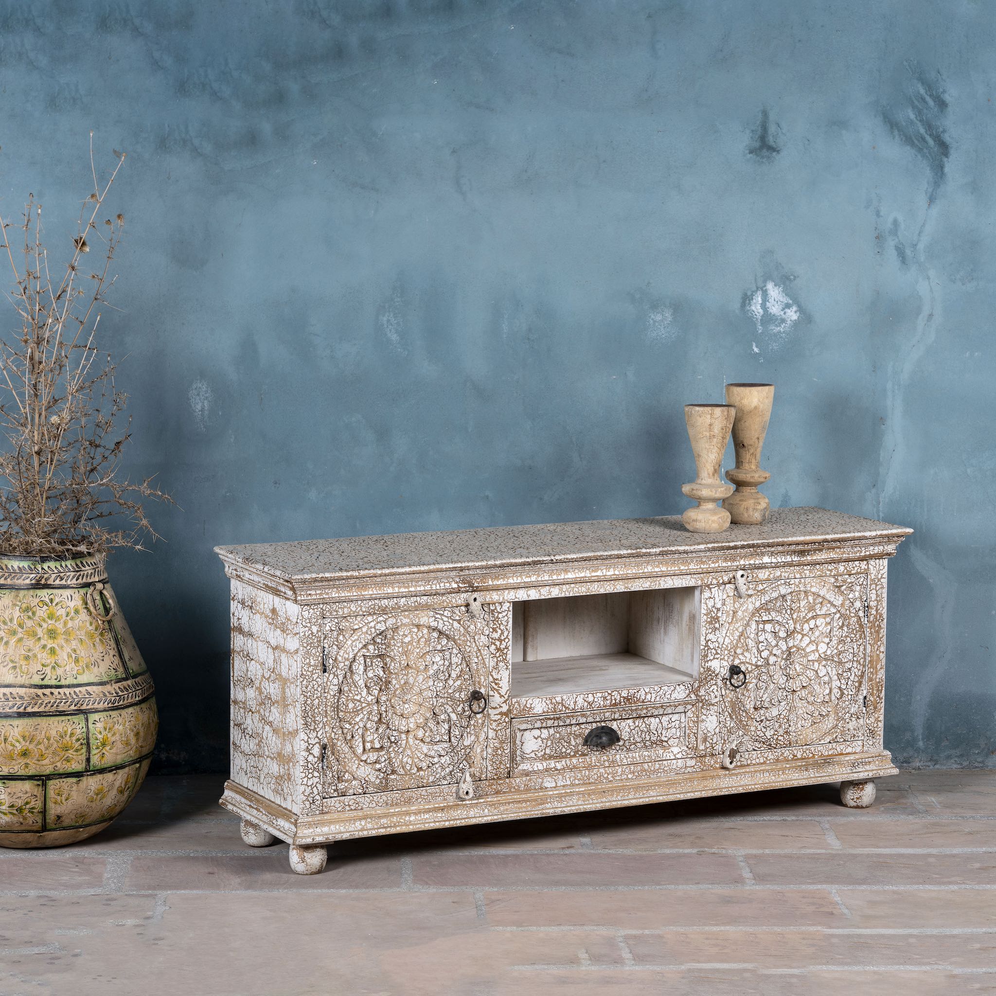 Decorative wooden TV stand against a textured blue wall with two vases on top.