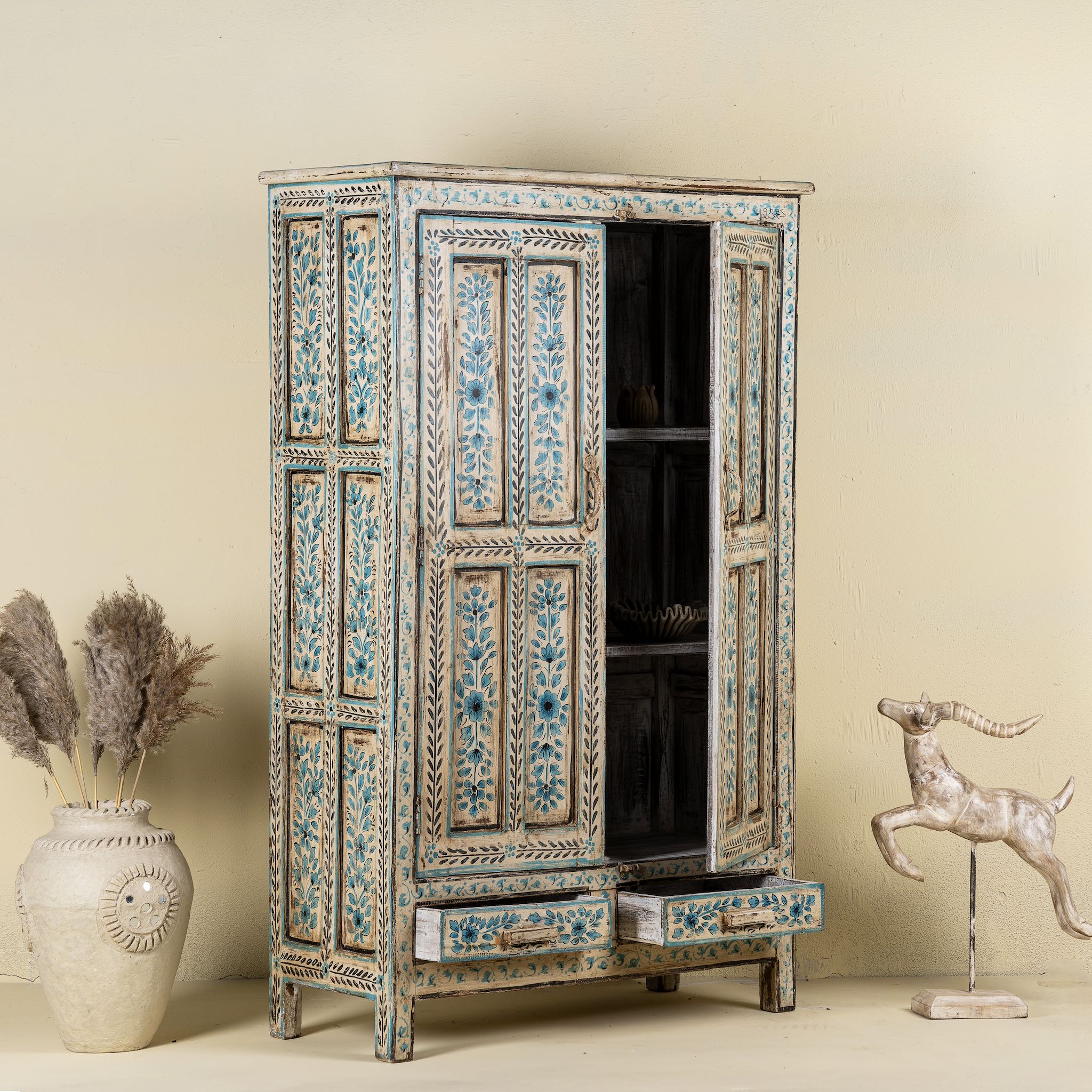 Open door image of a tall cabinet made from reclaimed wood, featuring hand-painted floral motifs in soft blue tones on panelled doors and drawers, with a distressed finish that adds vintage charm and highlights its artisanal craftsmanship.
