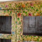 Close up image image of an and-painted floral showcase cabinet made from reclaimed wood with glass panelled doors and vintage rustic finish.
