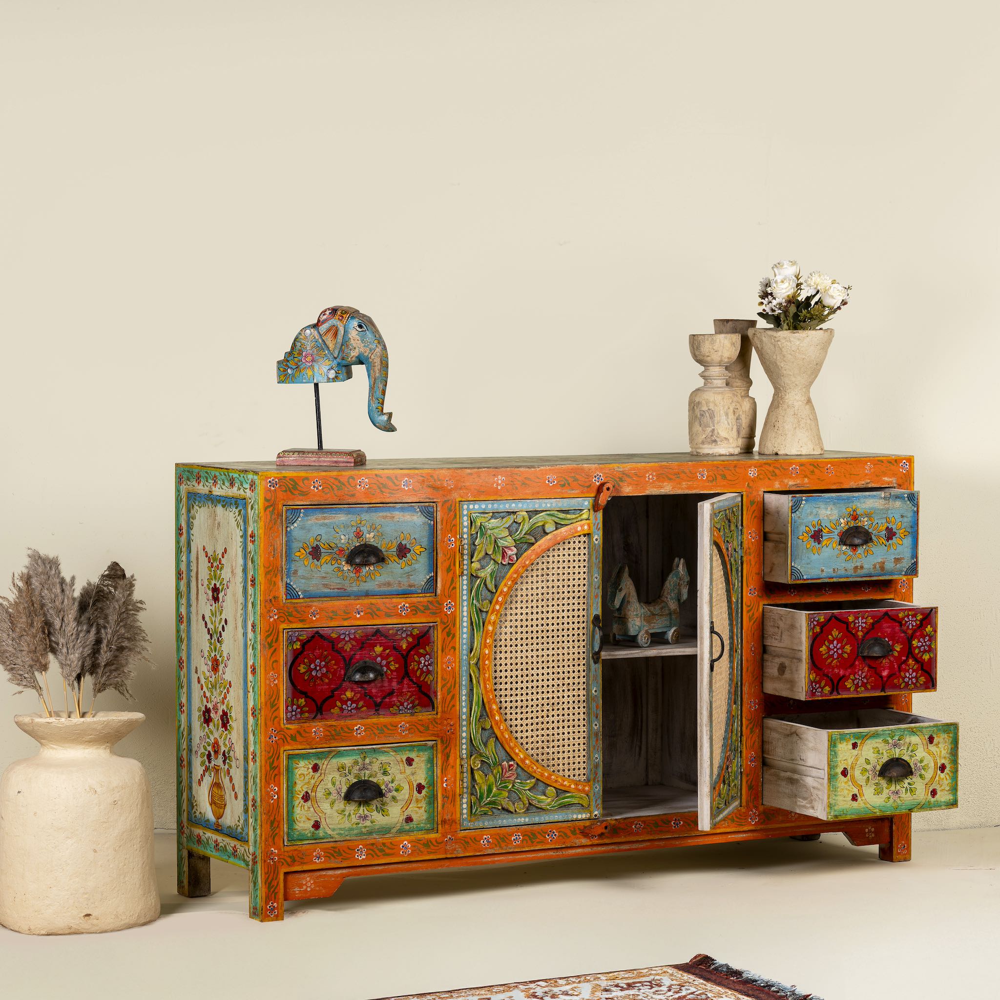 Side angle image with open drawers of a vintage style furniture sideboard with hand-painted floral motifs and rattan door inserts, bohemian rattan door furniture, 160 × 40 × 90 cm.