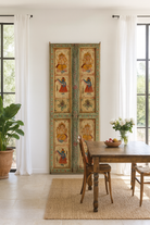 Lifestyle image of a Aum hand-painted teak door panel featuring Goddess Lakshmi and traditional dancers, framed by leafy green carvings—a spiritual and unique Indian wall decoration repurposed from antique teak architecture.