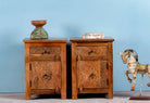Two hand-carved mango wood bedside tables with floral patterns against a blue background.