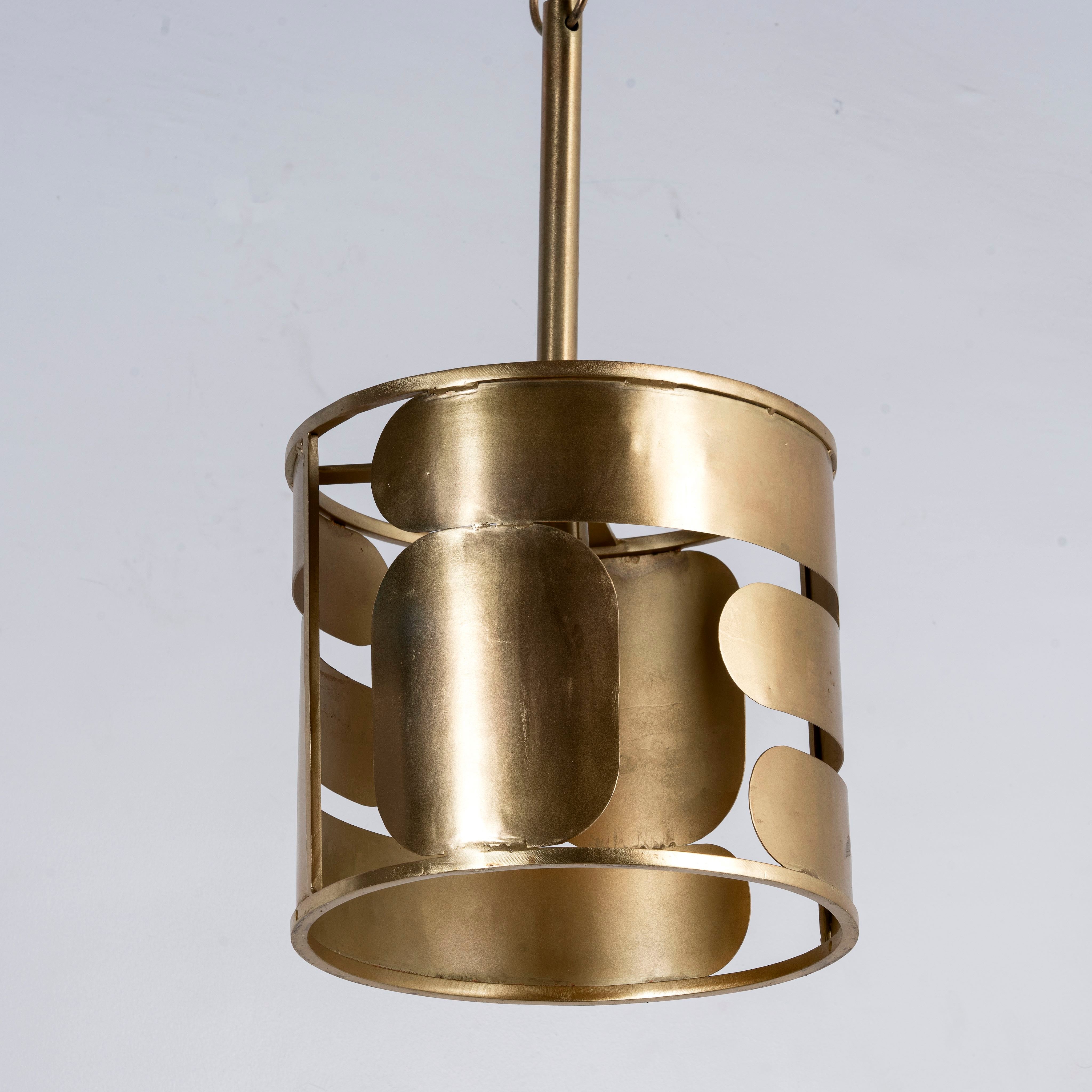 Side angle image of a medium round brass-plated metal pendant lamp with geometric cutout design – a modern take on vintage lights perfect for dining rooms, kitchens, or stylish living areas.