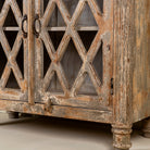 Close up image of the leg part of a handcrafted showcase cabinet made from reclaimed wood, featuring diamond-pattern glass pane doors, a crackled paint finish in earthy tones, two drawers, and vintage-inspired detailing.