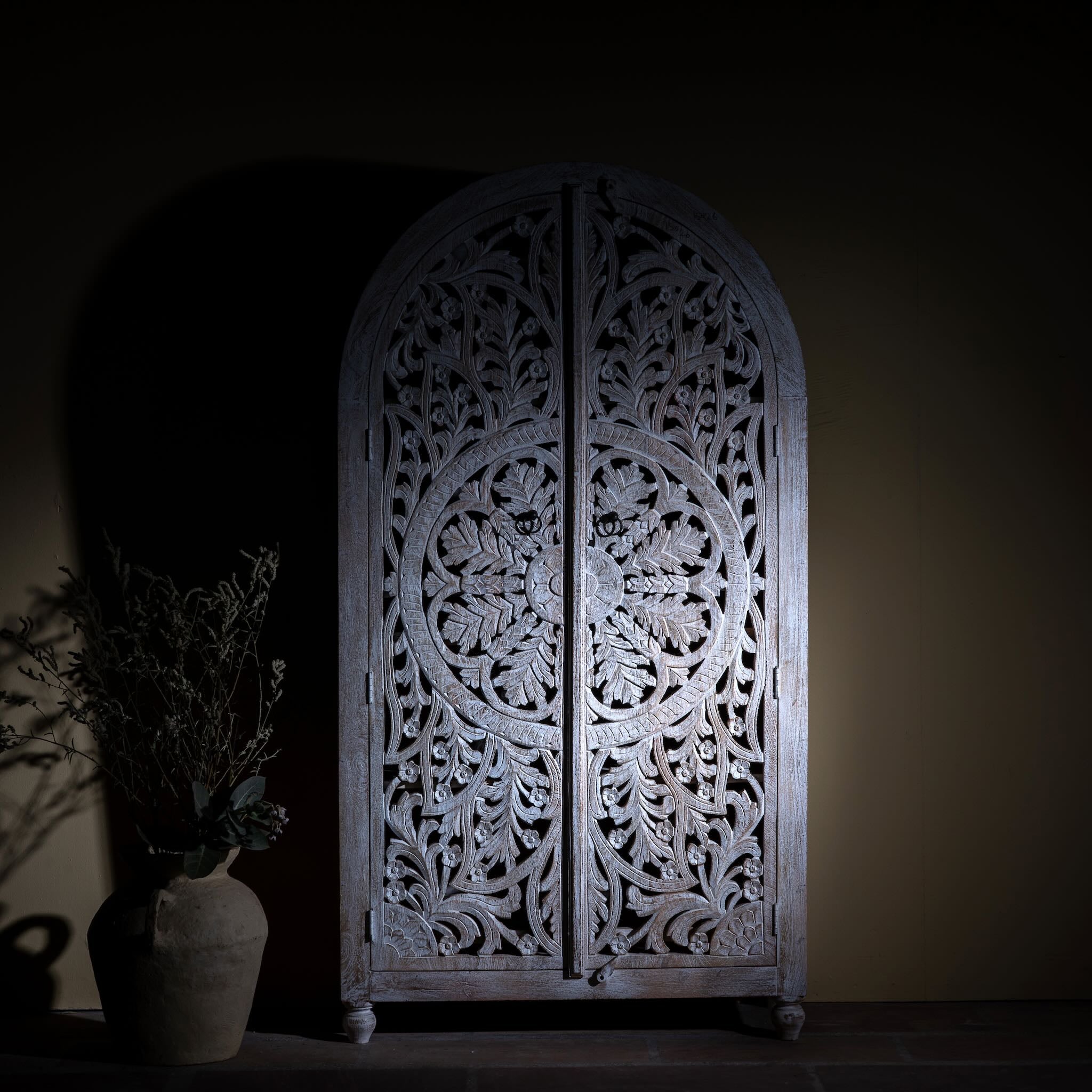 Lifestyle image of a Bhuvana arched mango wood wardrobe featuring a sculptural half-round design, intricate hand-carved floral detailing, and carved legs—an artisanal piece in the collection of arched wardrobes and mango wood wardrobes.