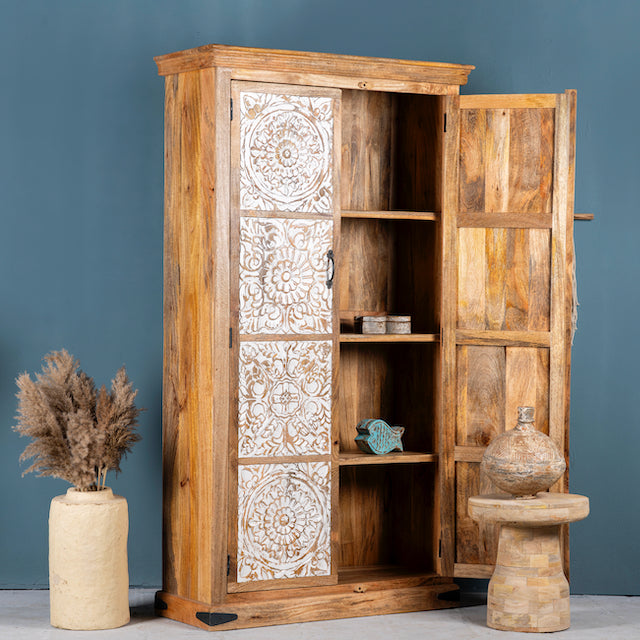 Side angle image with open door of a mango wood wardrobe with whitewashed floral carvings, vintage furniture cabinet in carved wood, 190 × 105 × 42 cm.