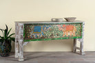 Side angle image of a hand-painted console table Caara made from reclaimed wood with vibrant elephant motifs and green foliage. A unique furniture piece full of vintage flair for bohemian interiors.