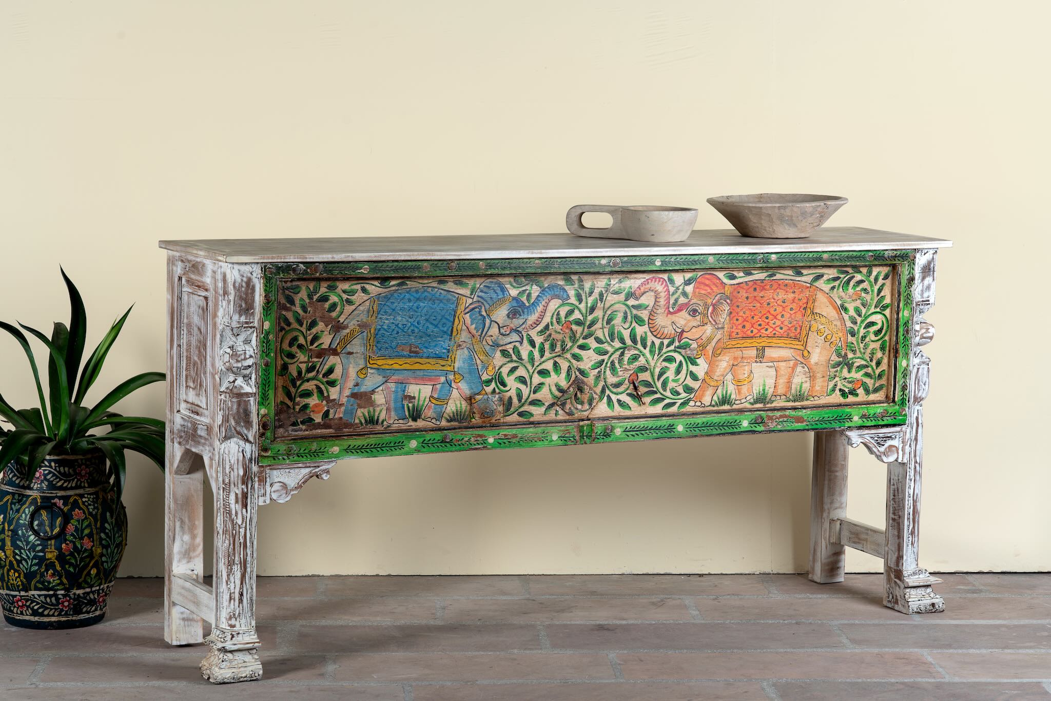 Side angle image of a hand-painted console table Caara made from reclaimed wood with vibrant elephant motifs and green foliage. A unique furniture piece full of vintage flair for bohemian interiors.