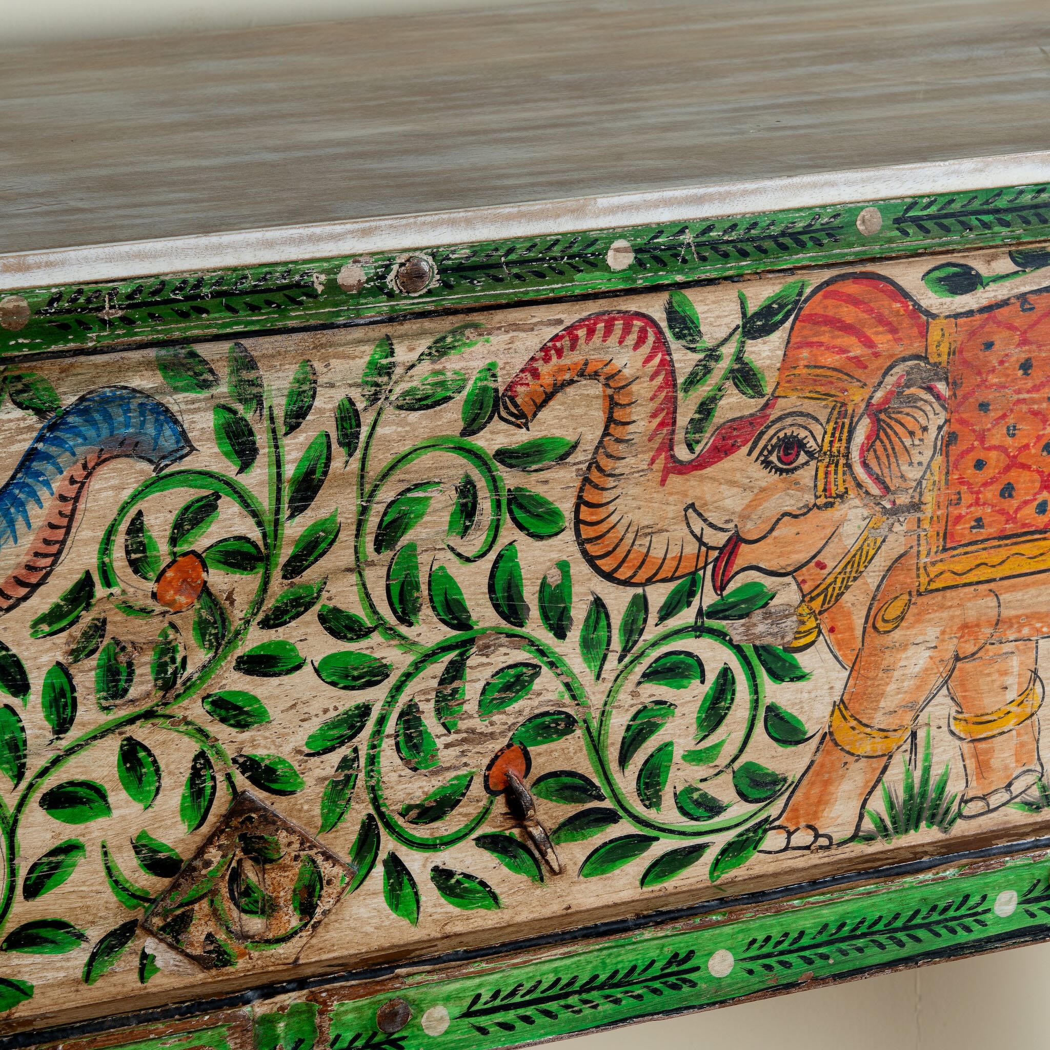 Close up image of a hand-painted console table Caara made from reclaimed wood with vibrant elephant motifs and green foliage. A unique furniture piece full of vintage flair for bohemian interiors.