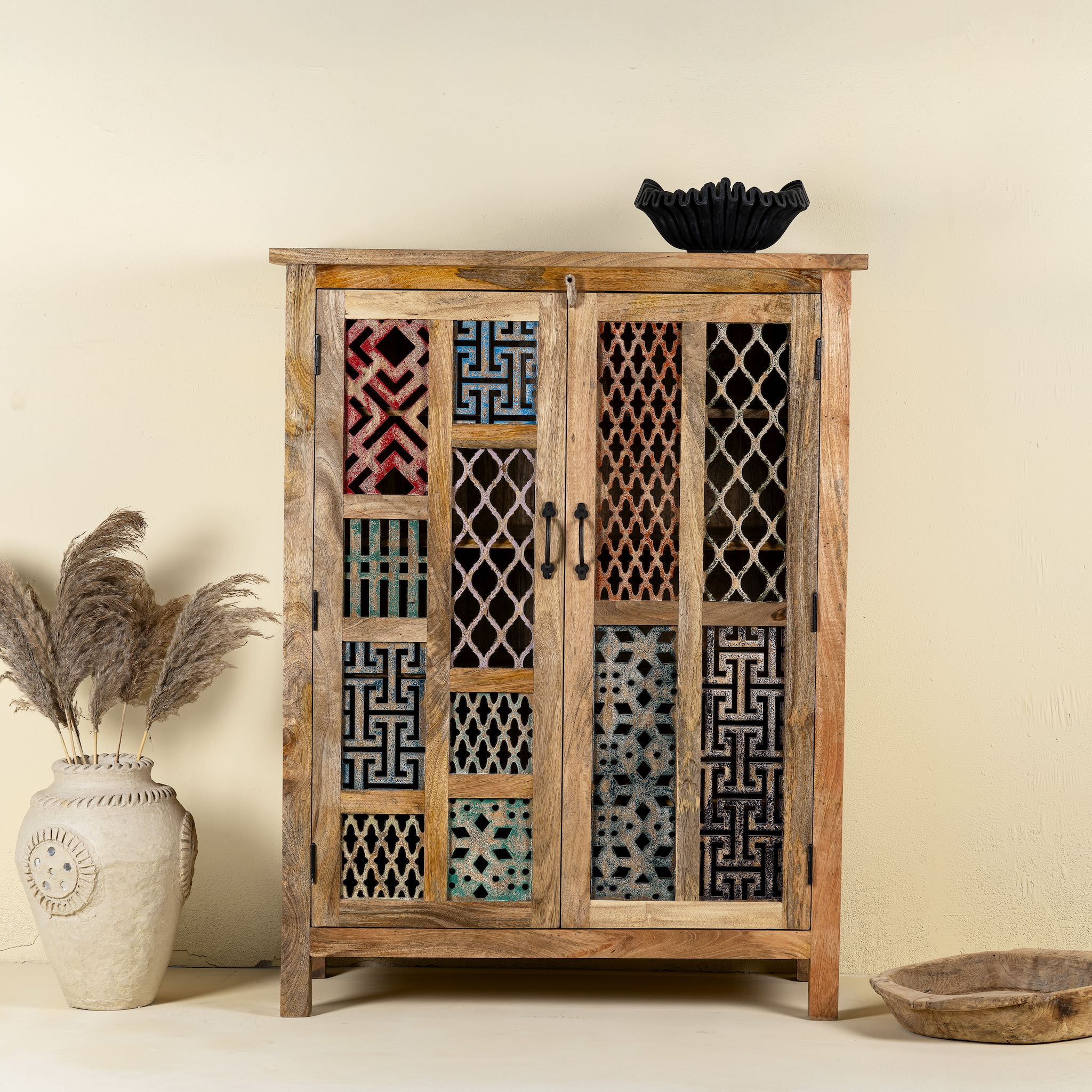 Front view image of a artisan-made cabinet crafted from mango wood, featuring double doors adorned with a patchwork of colourful, intricately carved geometric panels, blending traditional craftsmanship with a vibrant, eclectic style.

