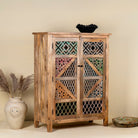 Side angle image of a handmade mango wood cabinet with carved floral and geometric lattice doors, distressed colour accents; artisanal furniture perfect for boho style interiors, 100 × 45 × 130 cm.