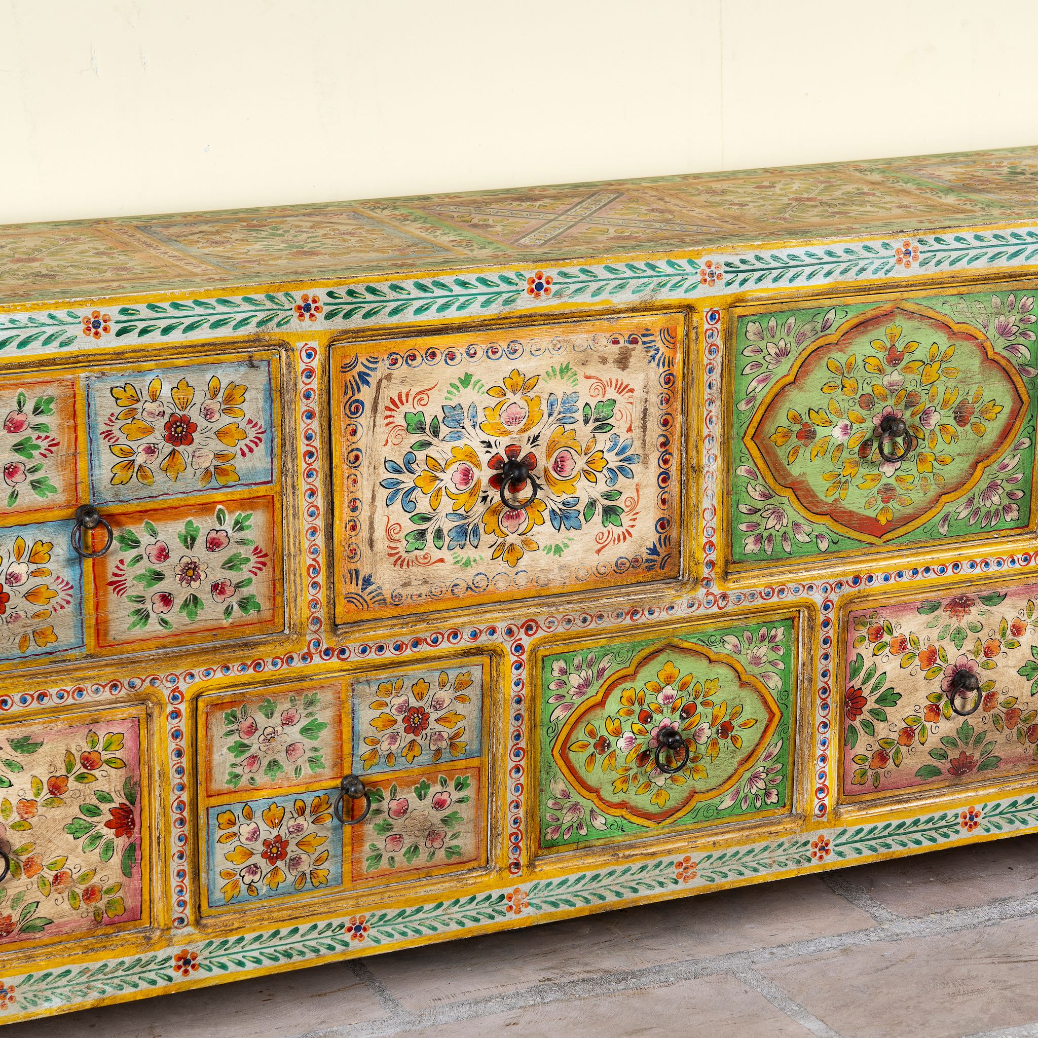 Close up image of a hand painted mango wood chest of 11 drawers with floral motifs; artisanal mango wood furniture and hand painted furniture, 250 × 41 × 85 cm.