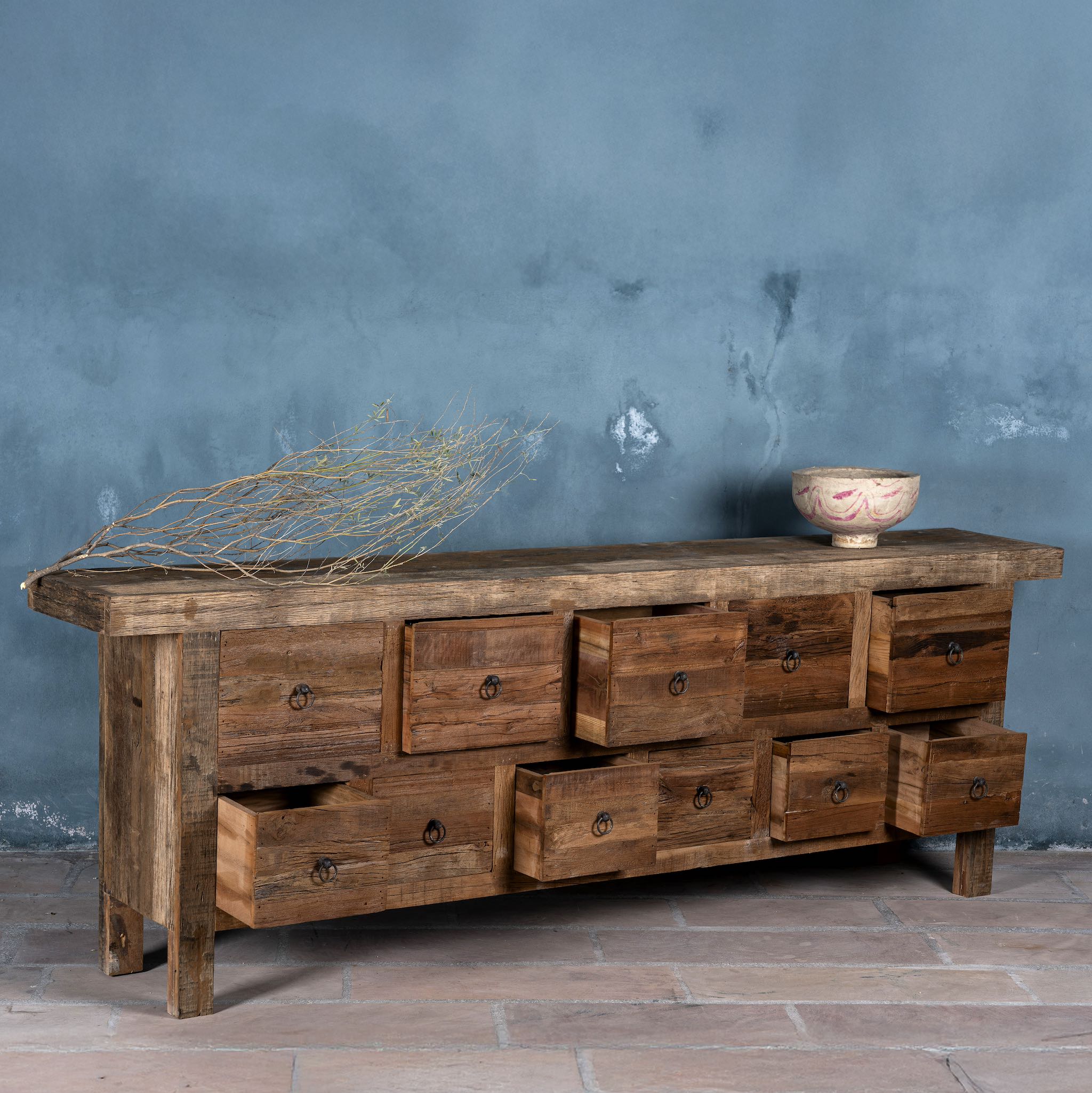 Side view image with open drawers of a large wabi-sabi style console table crafted from reclaimed wood, featuring a natural weathered finish and multiple drawers with simple metal ring pulls, embracing rustic imperfection and minimalist charm.
