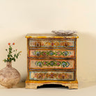 Front view image of a hand-painted chest of drawers made from reclaimed wood, featuring a vibrant floral motif across its four drawers, with a distressed finish and colourful detailing that highlights its vintage, artisanal charm.
