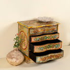 Side angle with open drawers image of a hand-painted chest of drawers made from reclaimed wood, featuring a vibrant floral motif across its four drawers, with a distressed finish and colourful detailing that highlights its vintage, artisanal charm.
