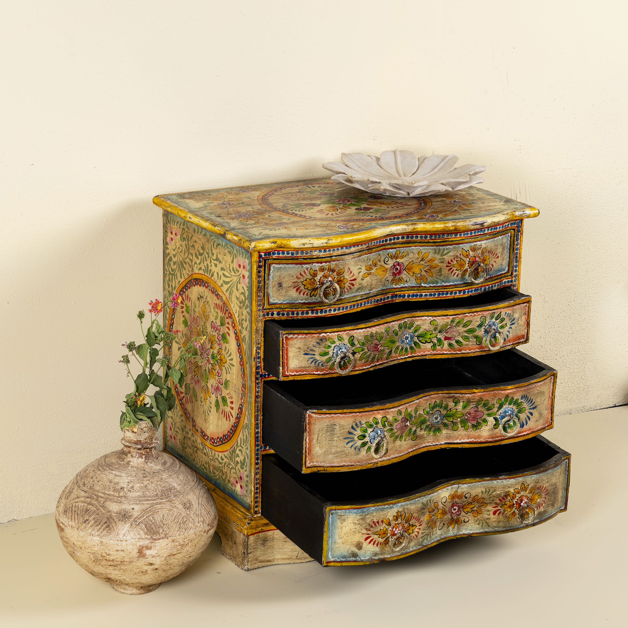 Side angle with open drawers image of a hand-painted chest of drawers made from reclaimed wood, featuring a vibrant floral motif across its four drawers, with a distressed finish and colourful detailing that highlights its vintage, artisanal charm.

