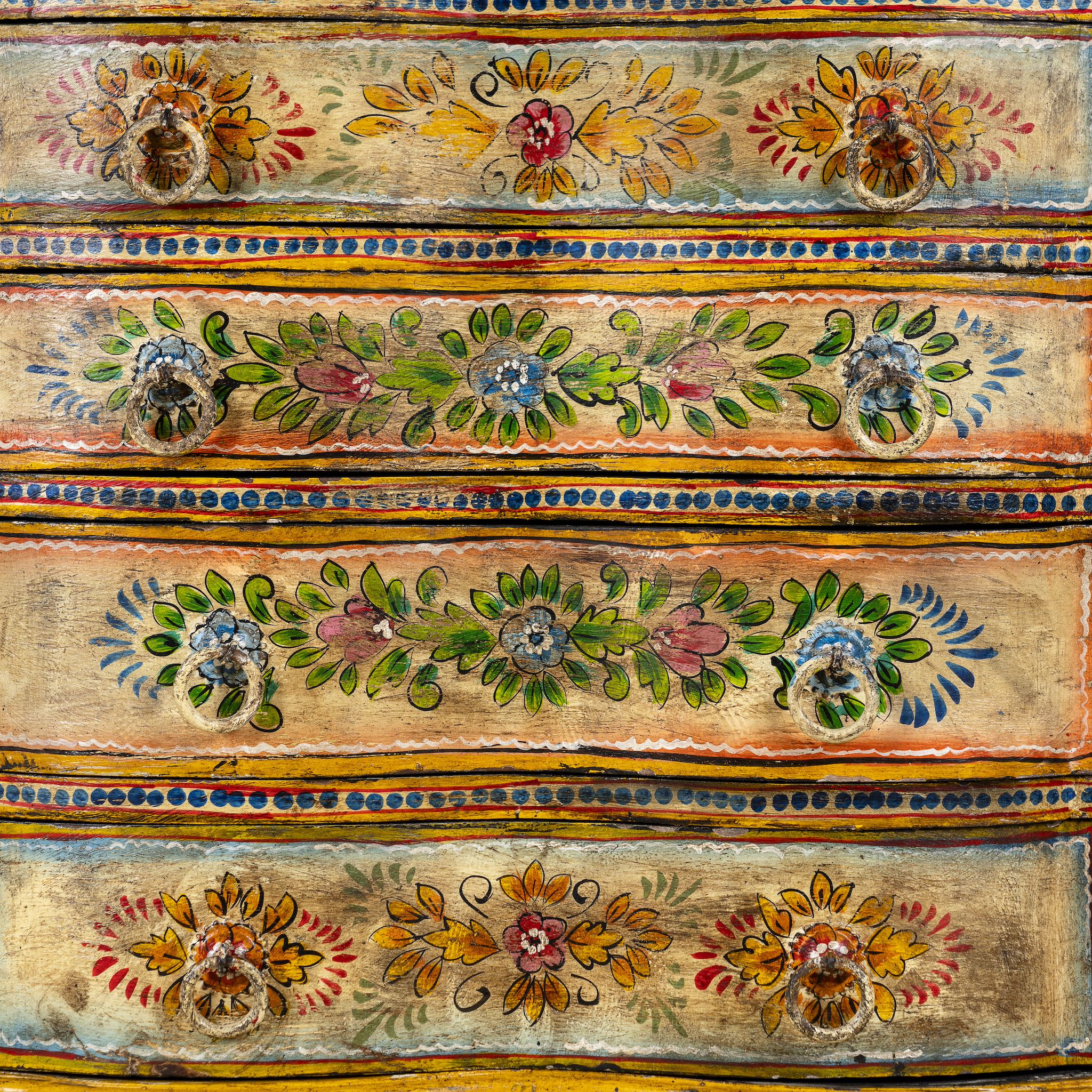 Close up image of a hand-painted chest of drawers made from reclaimed wood, featuring a vibrant floral motif across its four drawers, with a distressed finish and colourful detailing that highlights its vintage, artisanal charm.
