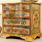 Close up side angle image of a hand-painted chest of drawers made from reclaimed wood, featuring a vibrant floral motif across its four drawers, with a distressed finish and colorful detailing that highlights its vintage, artisanal charm.
