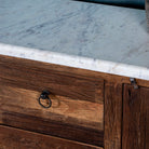 Close up picture of a driftwood sideboard with iron handles, 3 drawers and 2 doors and a slidable marble top in a maritime scene.