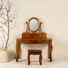 A handcrafted mango wood cosmetic table with a curved mirror and a matching chair, placed against a neutral background with a decorative branch in a vase to the side.