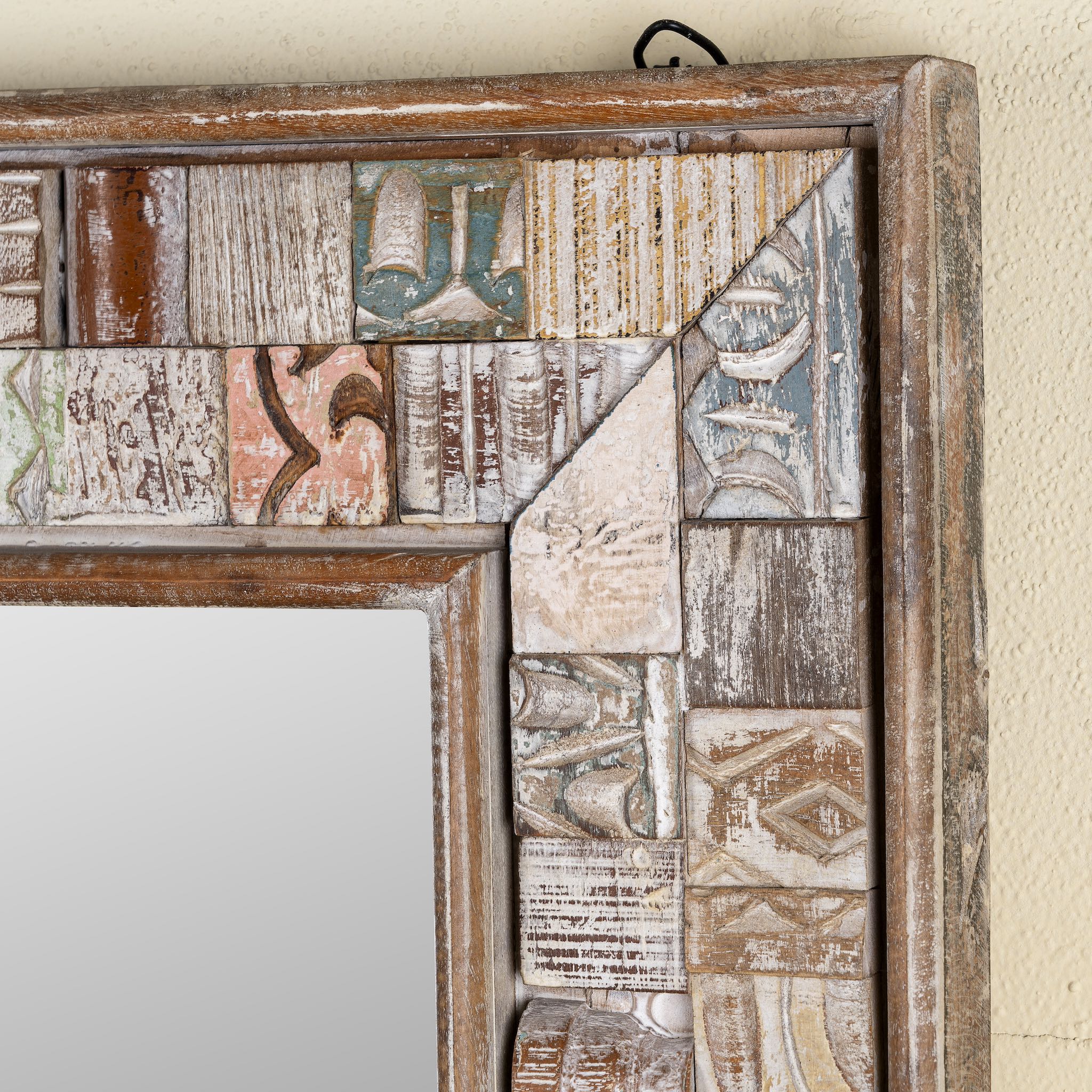 Close up image of a rectangular mirror framed with reclaimed wood, featuring a mosaic-style border of intricately carved and coloured wooden tiles, each with unique textures and patterns, creating a rustic and artistic statement piece.
