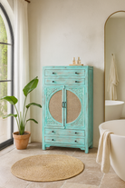 Lifestyle imagination of a vintage furniture cabinet in turquoise-washed mango wood with rattan door panels and hand-carved engravings, 80 × 148 × 40 cm.