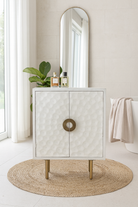 Lifestyle imagination of a carved wood furniture cupboard in white mango wood with hammered pattern, brass iron base, 88 × 43 × 122 cm.