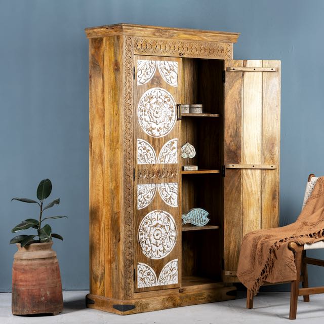 Side angle image with open door of a carved wood furniture wardrobe made from mango wood with whitewashed floral doors, wooden wardrobe in Ibiza-inspired style, 100 × 40 × 180 cm.