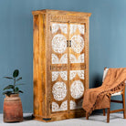 Side angle image of a carved wood furniture wardrobe made from mango wood with whitewashed floral doors, wooden wardrobe in Ibiza-inspired style, 100 × 40 × 180 cm.