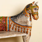 Close up image of the head of a hand-painted bench made from reclaimed wood, designed with intricately carved double horse heads at each end, featuring a vibrant floral backrest and detailed decorative patterns, blending traditional craftsmanship with whimsical artistry.
