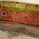 Close up image of a hand-painted bench made from reclaimed wood, designed with intricately carved double horse heads at each end, featuring a vibrant floral backrest and detailed decorative patterns, blending traditional craftsmanship with whimsical artistry.
