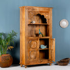 Side angle image with open doors of a hand-carved mango wood shelf with floral detailing, open shelf, and carved legs – carved wooden furniture in honey finish for rustic and Mediterranean interiors.