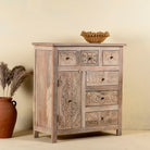 Side view of a hand carved mango wood cupboard with 6 drawers and 1 door, iron fitted door knobs and floral carvings.
