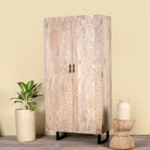 Side angle image of a hand-carved mango wood wardrobe with sandblasted finish and iron stand; artisanal bedroom furniture, 90 × 46 × 183 cm.