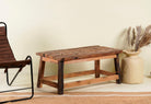 Side angle image of a rustic-style coffee table made from driftwood, showcasing a textured, uneven surface with natural wood tones and grain variations, supported by a sturdy, simple wooden frame, styled in a cozy minimal setting with neutral decor.

