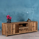Side view image of a large sideboard in Driftwood/ Wabi Sabi style made from recycled old wood, featuring four cabinet doors, two central drawers, and an open shelf with a naturally aged, rustic finish.

