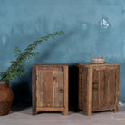 Side view of a pair of night stands in rustic minimalistic design with iron door handles decorated in front of a blue wall.
