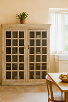 Lifestyle imagination of a tall reclaimed wood cabinet in sandblasted vintage design with glass-paneled doors; rustic living room furniture, 100 × 40 × 190 cm.