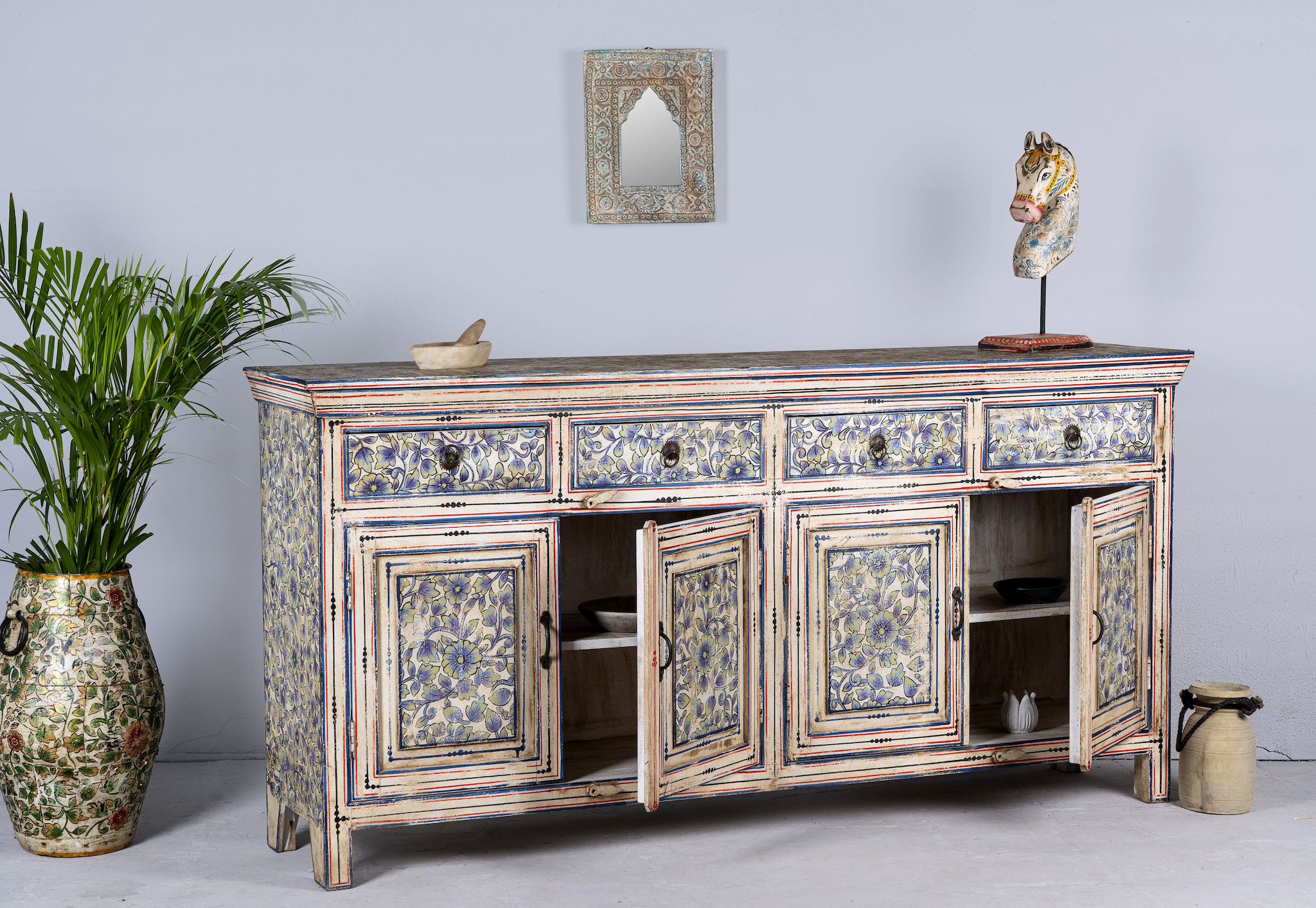 Side angle image with open doors of a vintage hand-painted floral sideboard with reclaimed wood frame, blue and yellow floral designs, and distressed multicolour detailing.