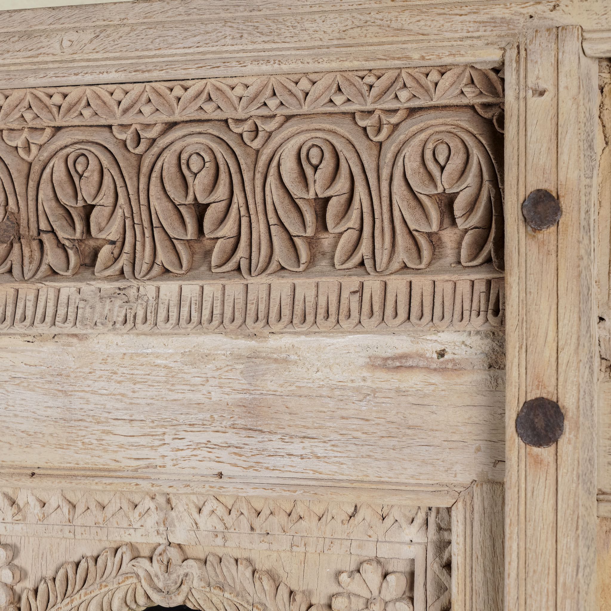 Close up image of a mirror stand crafted from reclaimed teak wood with intricate carved detailing and two storage cabinets, set on a sturdy iron base, blending rustic charm with vintage Indian architectural elements.
