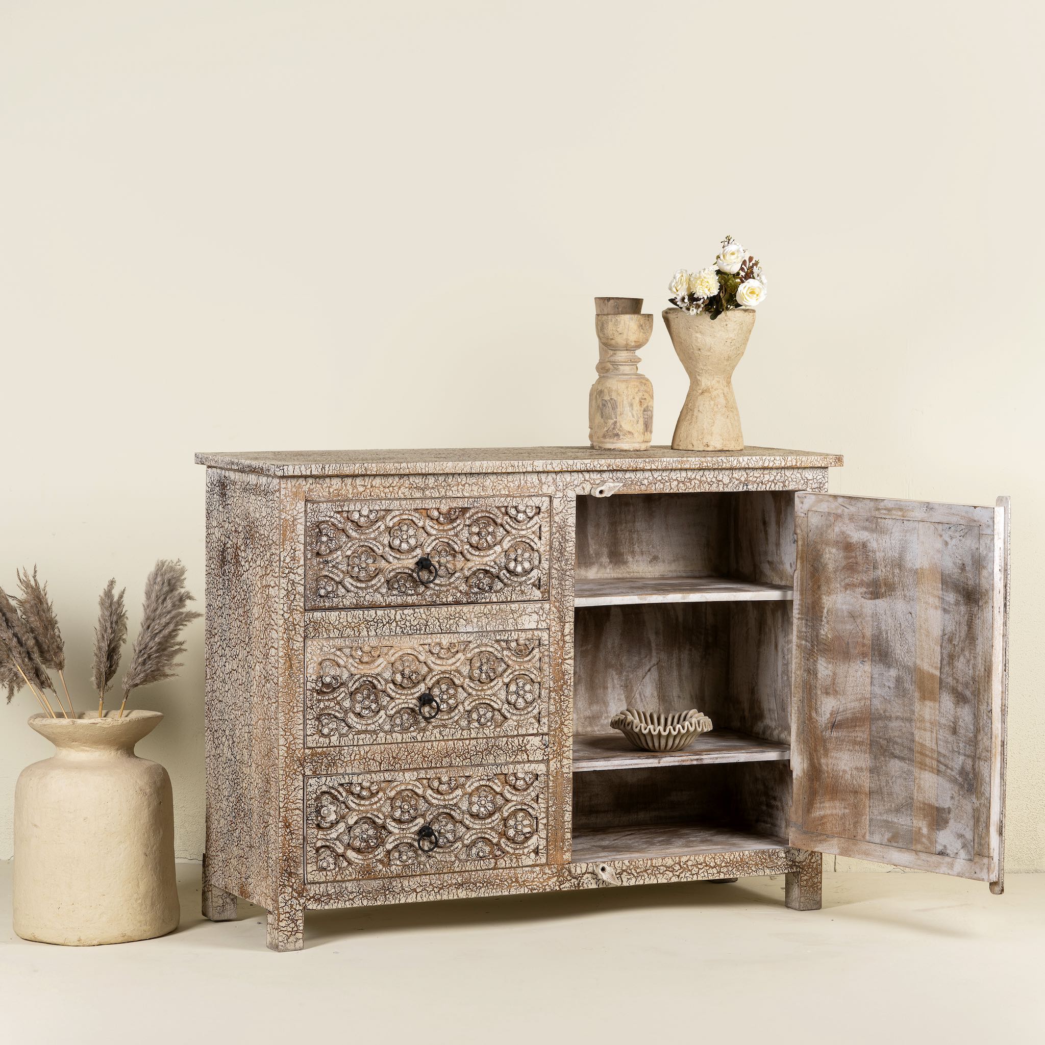 Open doors image of a hand-carved sideboard made from mango wood, featuring intricate geometric and floral patterns across the drawers and cabinet door, with a distressed whitewashed finish that enhances its vintage artisanal appeal.

