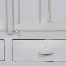 Close up image of a shabby chic teak wood cabinet with glass doors, drawers, and compartments – sustainable living room furniture crafted from refurbished teak wood with a soft white finish.