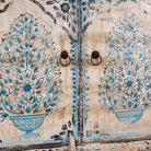 Close up picture of a vintage-style cabinet made from reclaimed wood, featuring intricate hand-painted floral vases in soft blue tones and distressed black detailing for an artisanal heritage look.