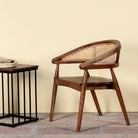 Lifestyle image of an acacia wood chair with curved frame and woven rattan backrest, elegant wooden armchair, 60 × 45 × 90 cm.