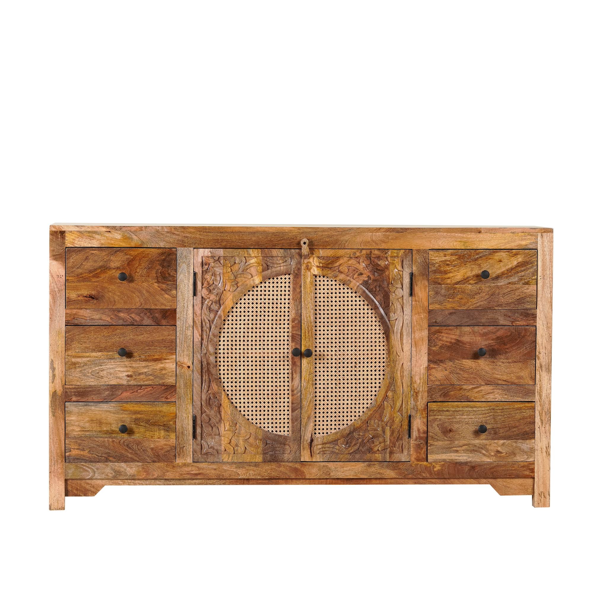 White background image of a hand-carved mango wood sideboard with rattan inserts, featuring two cabinet doors with rattan fronts and six drawers, placed against a neutral backdrop with decorative items on top.