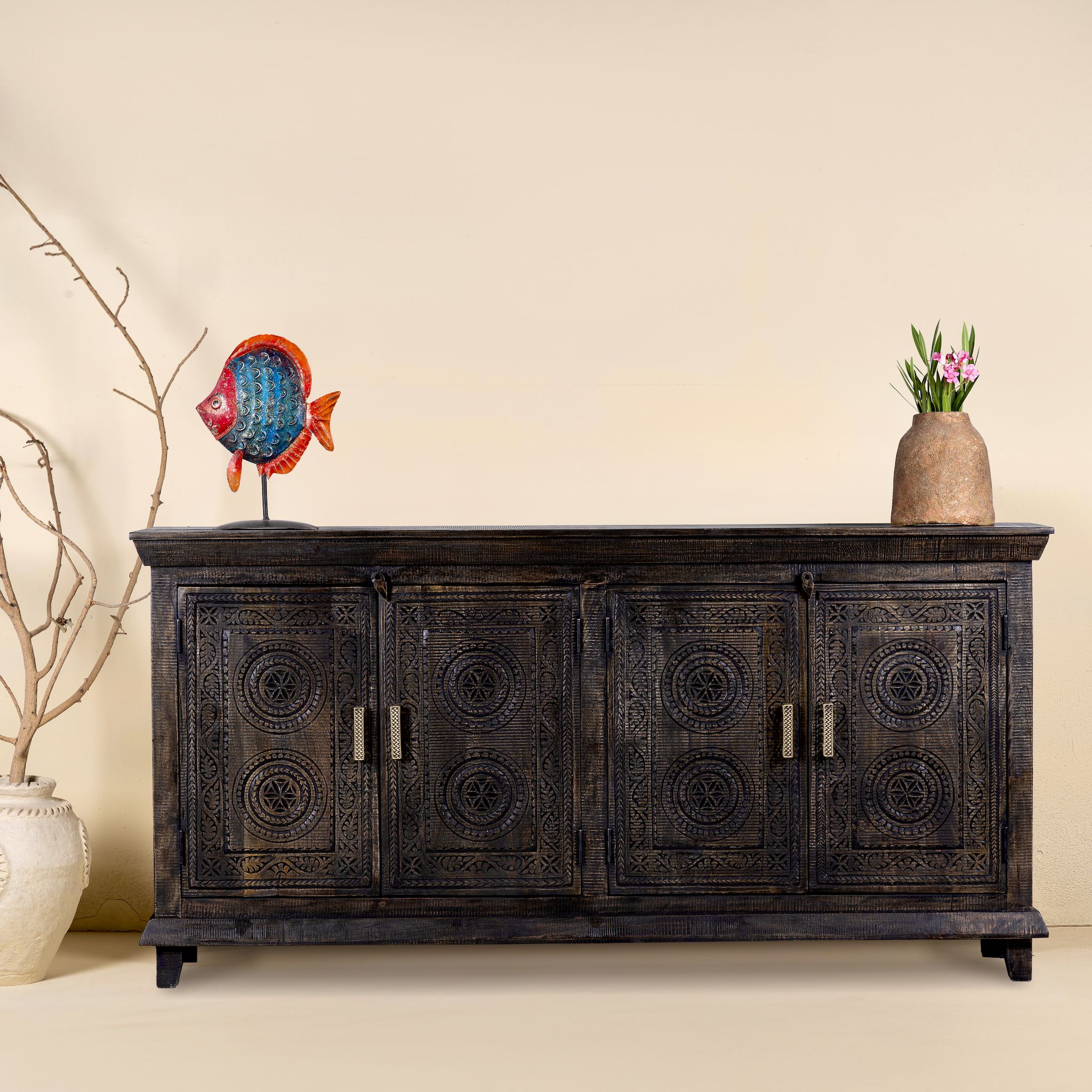 Black mango wood sideboard with intricate hand-carved geometric patterns and four cabinet doors, styled with decorative accents on top.