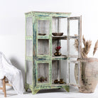 Side angle image with open door of a refurbished teak wood showcase with distressed green finish – sustainable furniture with boho style interior appeal and glass-panelled storage.